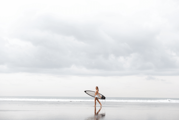 sober living houses pb surfer grey day sea woman shoreline blue sand walking