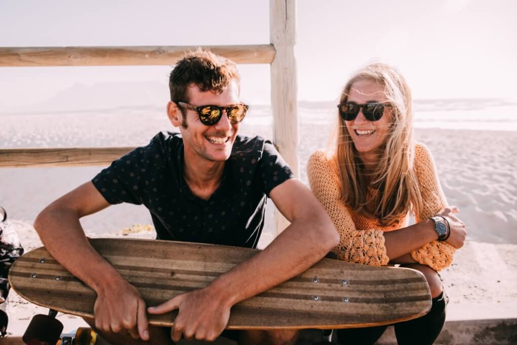 Couple walking with skateboards along the Pacific Beach boardwalk, smiling at each other in afternoon light