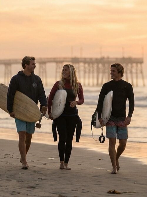 Young adults from a sober living by the sea community carrying surfboards toward the Pacific Beach pier at sunrise